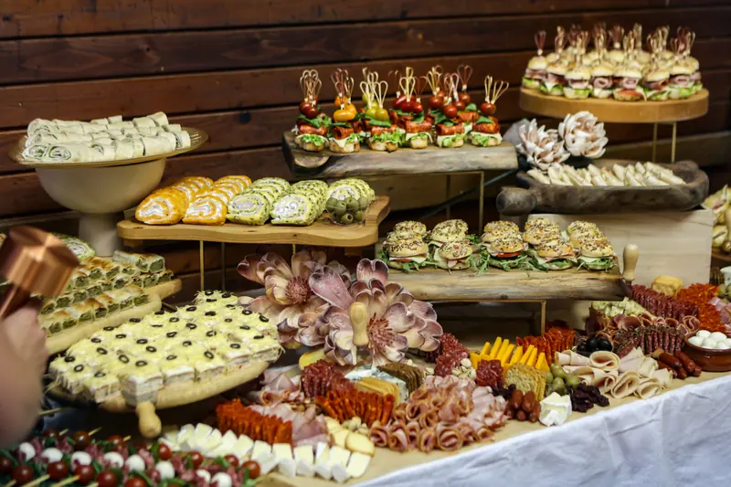 A grazing table of rolled wraps, mini sandwiches, skewers, cheeses and cold meats on wooden boards